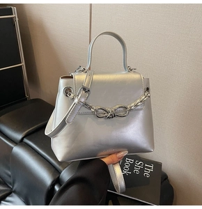 Detail of silver metallic handbag with thick chain knot and branding on leather sofa