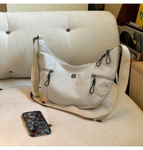 Détail du sac hobo en nylon gris avec poches zippées sur un canapé en velours