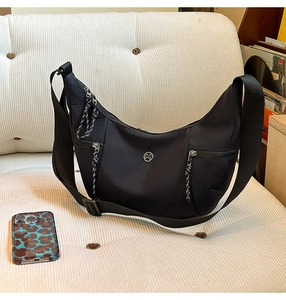 Détail d'un sac demi-lune en nylon noir avec logo M métallique et fermetures éclair tressées
