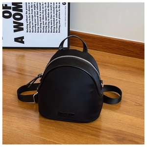 Detail of a black nylon mini backpack featuring a silver zipper and a metal logo plate