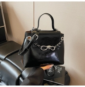 Close-up of a glossy black leather shoulder bag with silver chain and bow buckle detail