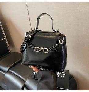 Detail shot of the glossy black crossbody bag featuring a silver metal chain and bow buckle