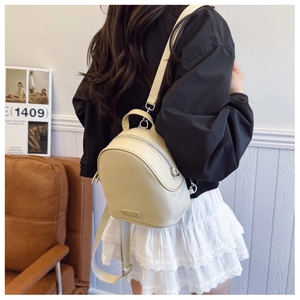 Detail of a beige faux leather mini backpack with silver zippers and a top handle
