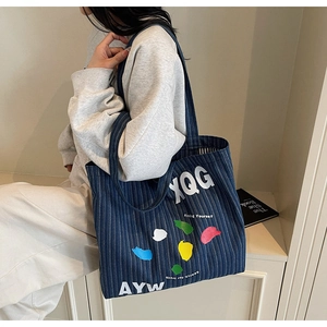 Detail of striped denim tote bag with colorful artistic graffiti and shoulder strap