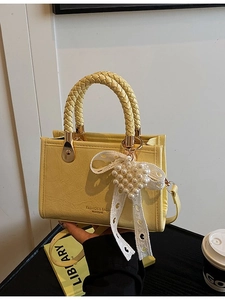 Yellow vintage crossbody bag with woven handle and pearl heart charm on a desk