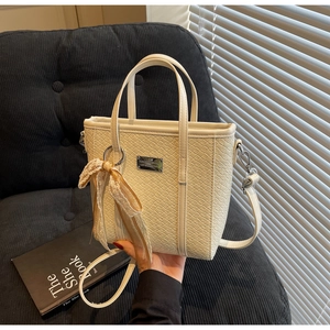 Dettaglio di una borsa tote intrecciata beige con logo in metallo e fiocco in pizzo