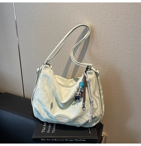 Detail of hobo shoulder bag featuring marble print, brand logo and decorative bear charm