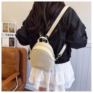 Detail of a creamy white mini backpack with silver zippers and a sleek metal logo plate