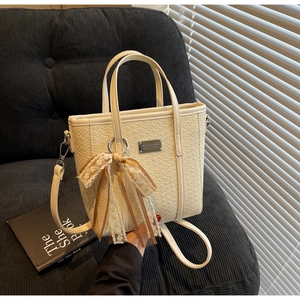 Dettaglio di una borsa intrecciata bianco crema con fiocco in pizzo e placca argento