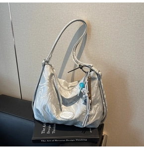 Detail of silver marble textured tote bag with trendy charms on black books background