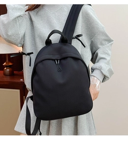 Minimalist black oxford fabric backpack worn by a model in a warm indoor setting