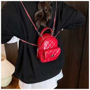 Detail of red quilted mini backpack with silver chain straps worn over black hoodie