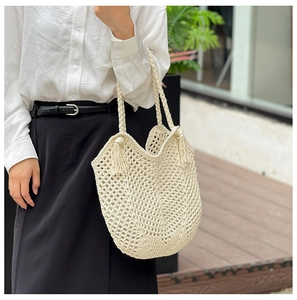 Détail d'un sac cabas tissé beige ajouré avec glands au style minimaliste français