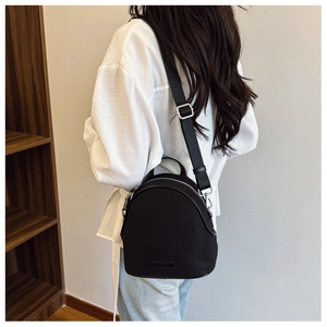 Detail view of a black shell-shaped mini backpack worn by a model in a cozy indoor setting