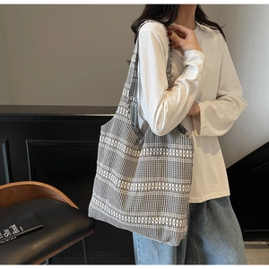 Close-up of black and white checkered canvas tote bag with white horizontal stripes on model