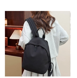 Rear view of model wearing a black Oxford cloth backpack with top handle in home setting