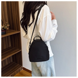 Side view of small black nylon backpack on model showing size and metal logo detail