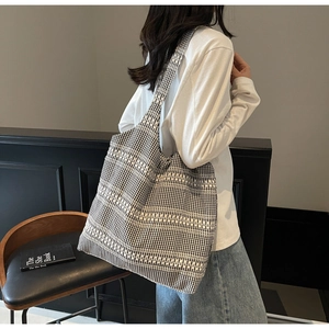 Detail shot of a black and white woven tote bag with wavy patterns and long shoulder straps