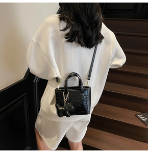 Détail du sac seau noir brillant avec motif lapin gaufré et accessoire de charme chiot