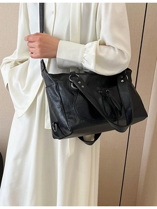 Black vintage leather tote bag with silver hardware worn by model in white dress