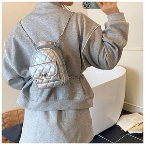 Detail shot of a mini silver quilted backpack with metal chains on a female model