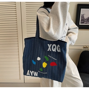 Detail of blue striped denim tote bag featuring large white letters and colorful pattern