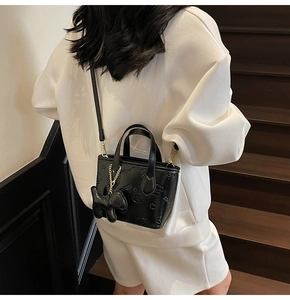 Détail du mini sac bandoulière noir embossé avec motifs mignons sur une tenue blanche