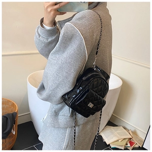 Detail of black quilted patent leather mini backpack with silver chain strap on model