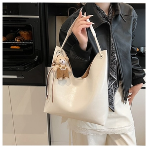 Close-up of cream white glossy leather tote bag with a cute bear charm in a kitchen setting