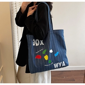 Detailed view of blue striped denim tote bag with colorful graffiti and XOG letter print