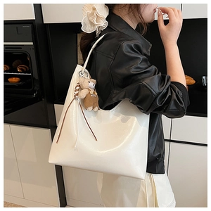 Detail of white patent leather tote bag with cute bear charm and woven tassel accent