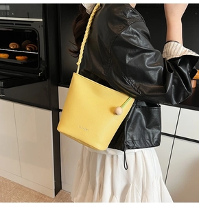 Detail of yellow bucket bag featuring lychee grain leather and woven shoulder strap