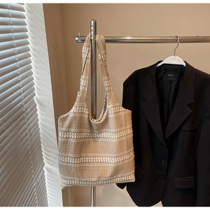 Detail of a brown and white gingham canvas tote bag hanging next to a black blazer