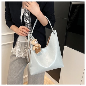 Detail of light blue glossy tote bag with cute plush bear charm on a female model