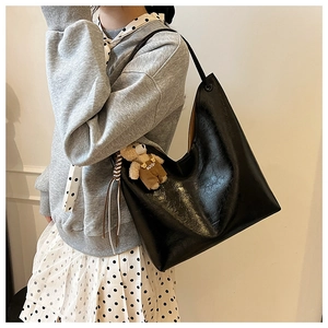 Detail of a black oil-wax leather shoulder bag with a cute bear plush pendant