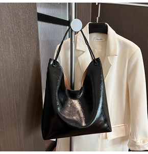 Detail of glossy black patent leather hobo tote bag with fine texture on metal stand