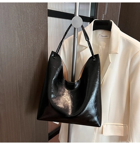 Detail of glossy black patent leather tote bag hanging on a rack with a white blazer