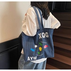 Detail of striped denim tote bag with colorful graphic prints and white typography