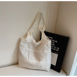 Detail of white canvas tote bag featuring pleated texture and hollow lace embroidery