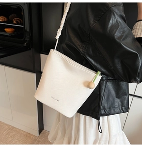 Detail of white lychee leather bucket bag featuring a thick woven strap and spherical charm