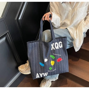 Detail of large denim tote bag featuring colorful graffiti prints and slogan stripes
