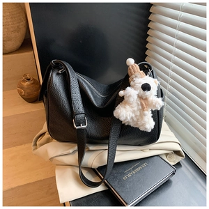 Detail of black lychee leather bag with a cute teddy bear charm and adjustable strap