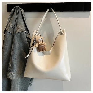 Detail of off-white faux leather tote bag featuring a cute teddy bear charm and sleek finish