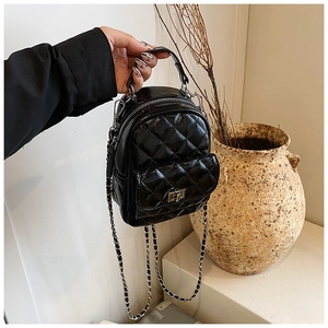 Detail of mini black quilted backpack featuring glossy finish and metal chain straps