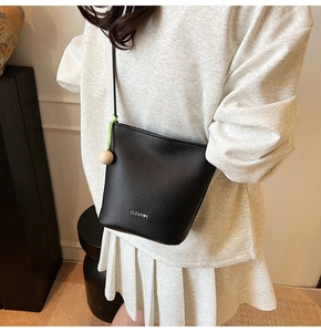 Detailed side view of black bucket bag featuring lychee texture and green cord accent