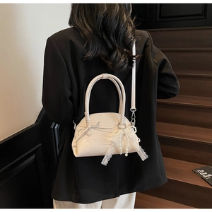 Borsa a tracolla bianca con fiocco in pizzo e perle mostrata da una modella sulle scale