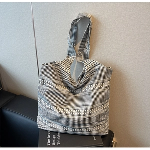 Detail of black and white checkered knit tote bag with jacquard stripes on a leather sofa