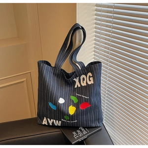 Detail of large denim tote bag with stripes and street style graphic prints on a leather chair