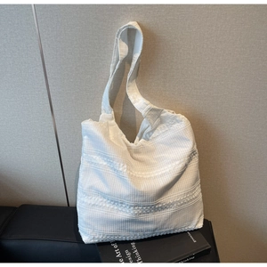 Detail of white canvas tote bag with pleated texture and woven stripes on a black sofa