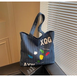 Detailed close-up of blue striped denim tote with artistic XQG graffiti and paint splash